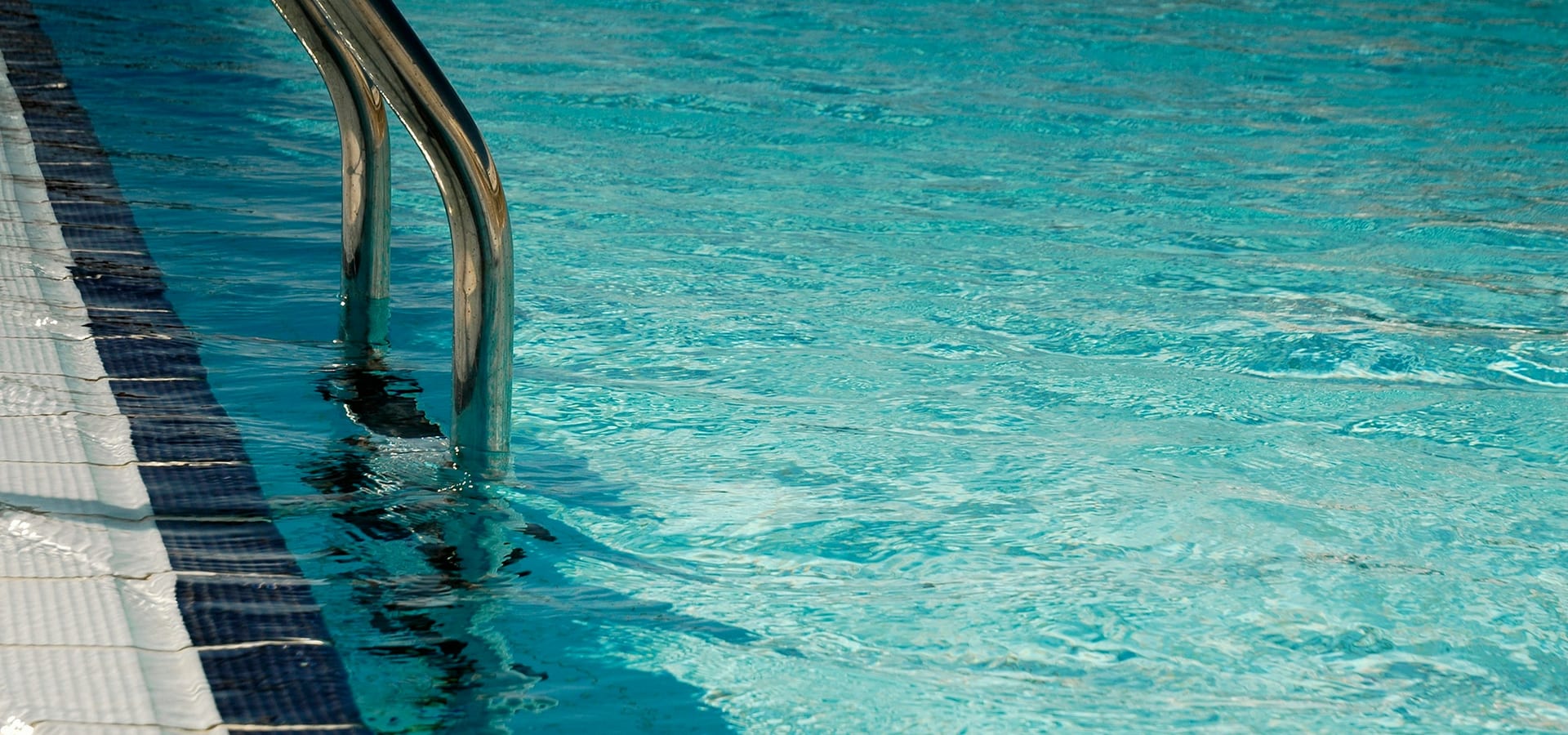 Clear turquoise pool water beside a stainless steel pool ladder